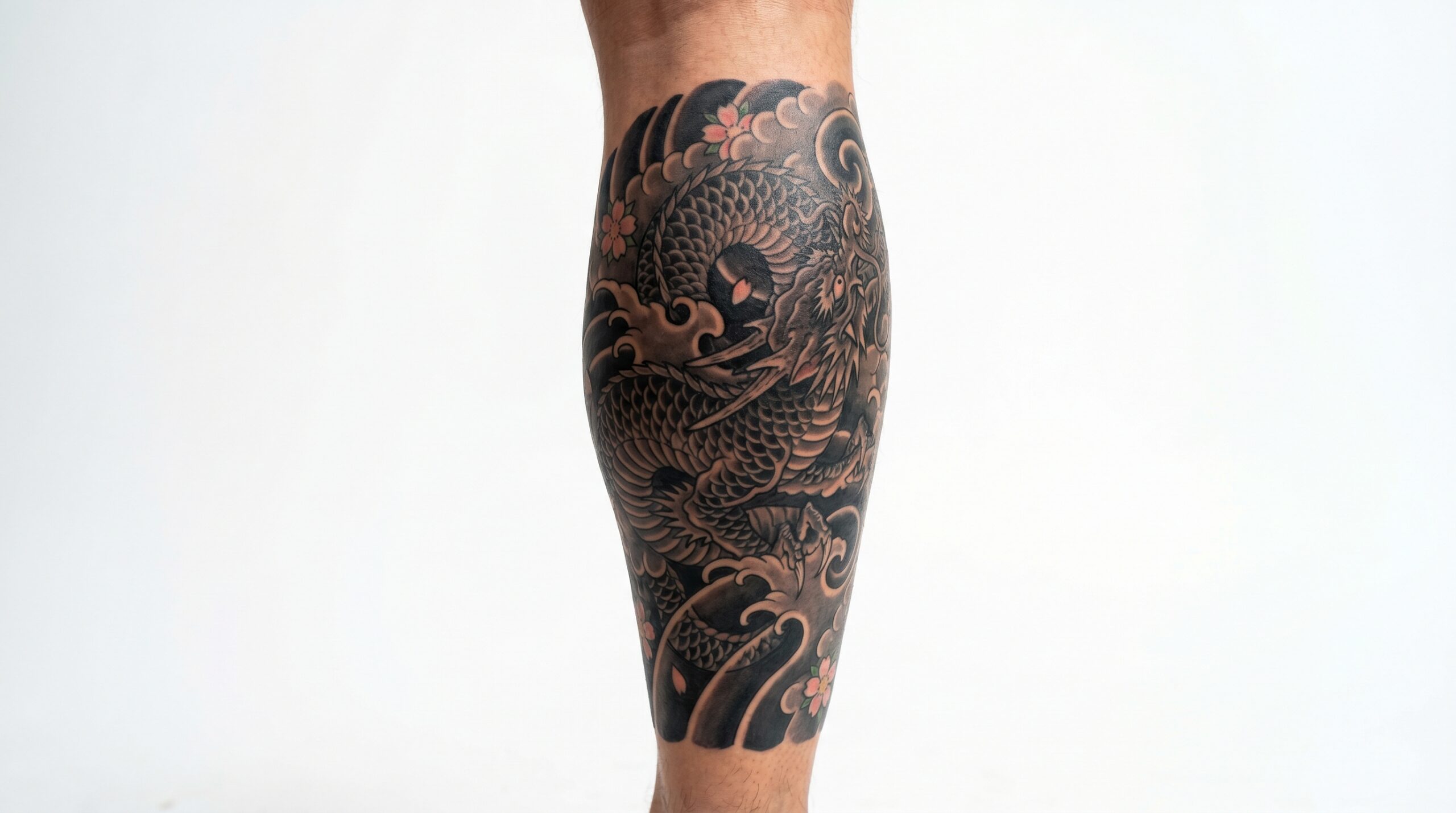 A powerful Japanese Traditional style tattoo fully wrapping around a man's muscular calf. The design features an energetic Ryu dragon navigating through bold black waves and soft grey clouds with scattered cherry blossoms.